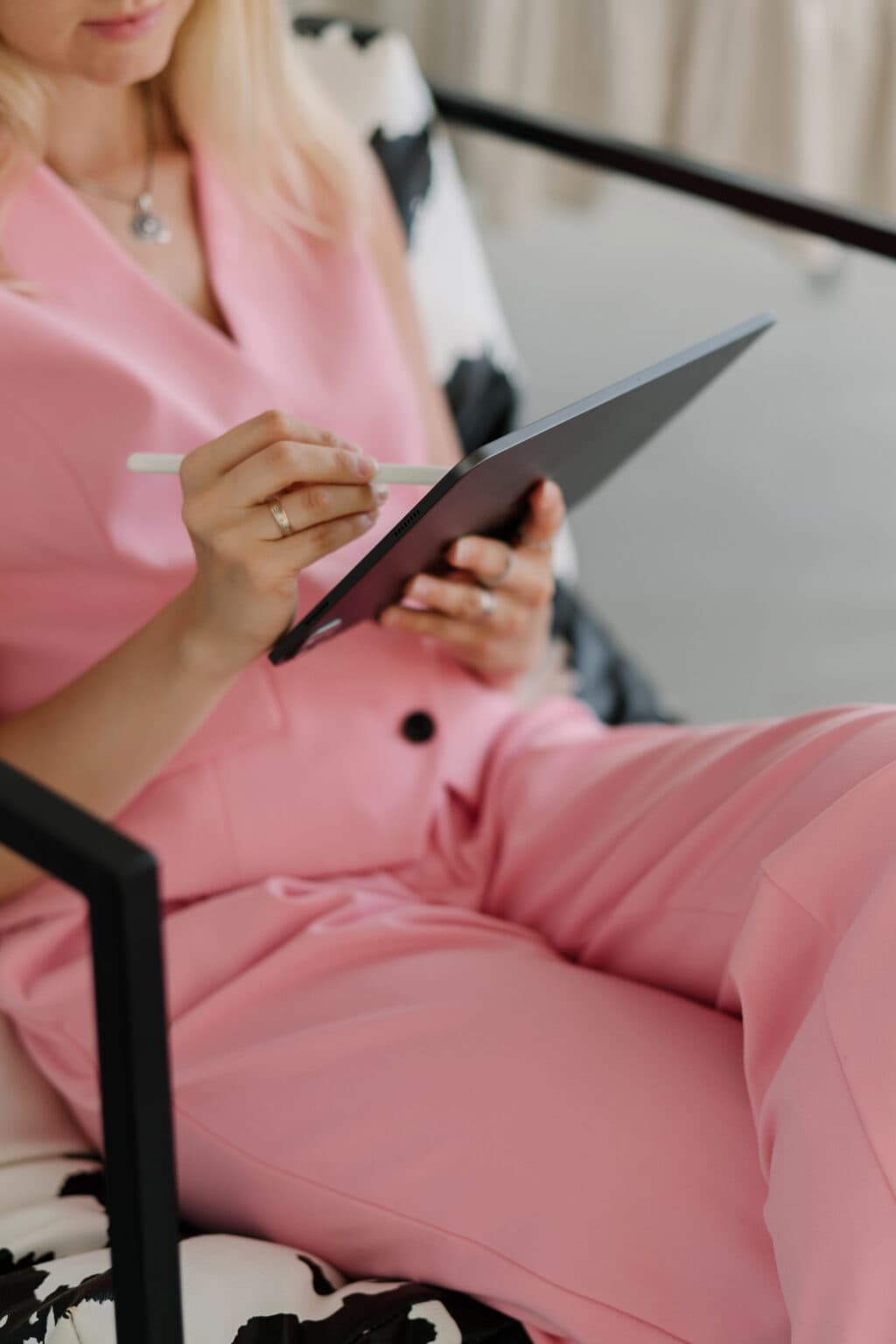 Woman in a pink suit sits on a chair, using a tablet with a stylus—perhaps reviewing copywriting services. Her face is partially out of frame.