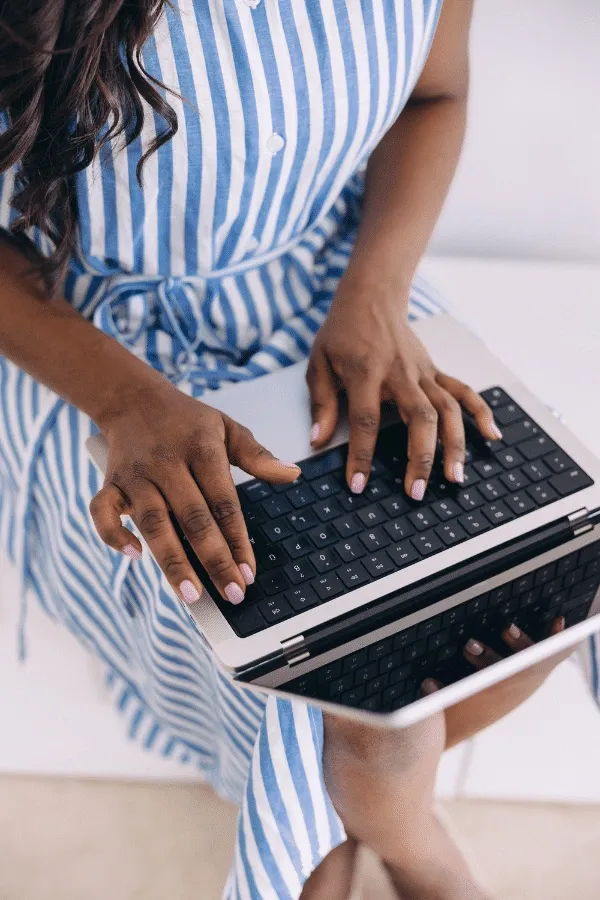 A person in a blue and white striped dress is typing on a laptop while seated.